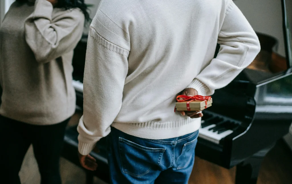 Uomo che nasconde un regalo a sorpresa dietro la schiena, davanti a una donna. L'idea regalo di natale è stata ideata da Gifting.